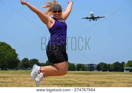 Blonde Adult Woman At Gravelly Point Park In Washington Dc Jumps As An Airplane Flies In For A Landi