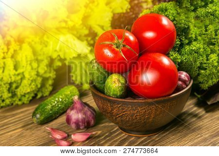 Tomatoes, Garlic Bulb And Cucumbers On A Wooden Table. Green Salad In The Background. The Concept Of