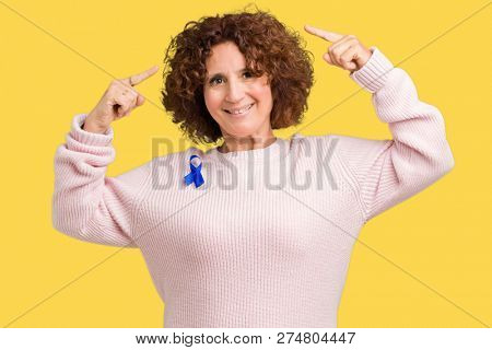 Middle ager senior woman wearing changeable blue color ribbon awareness over isolated background Smiling pointing to head with both hands finger, great idea or thought, good memory