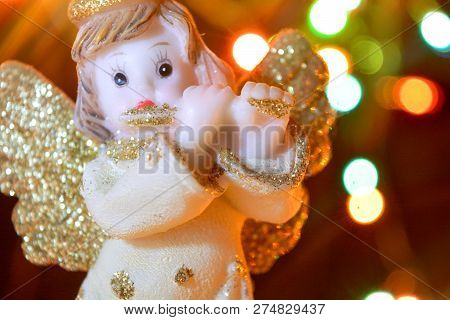 Figurine Of Little Angel With Golden Shiny Wings And Halo That Plays Flute On Shining Background Of 