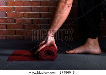 Man Twists Yoga Mat Closeup On Brick Wall Background