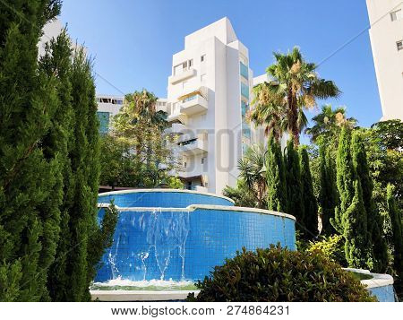 Residential Buildings And Fountain Surrounded With Green Plants In  Rishon Le Zion.