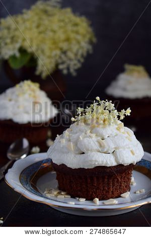 Chocolate Capcakes With Vanilla Cream Sprinkled With White Chocolate And Elderberry Flowers. Vintage