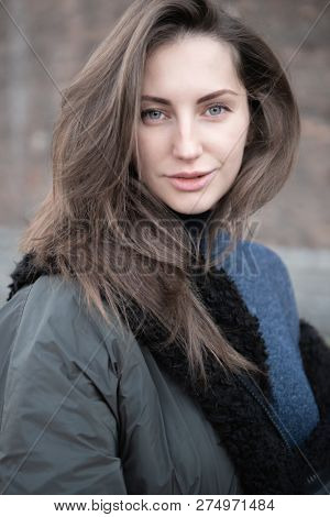 Attractive young woman wearing gray dress and hakki jacket with long fair hair posing outdoor. Beautiful caucasian model portrait.