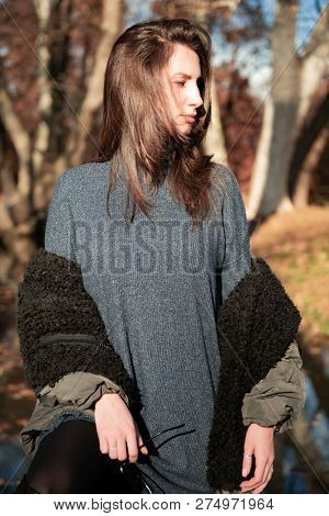 Attractive young woman wearing gray dress and hakki jacket with long fair hair posing outdoor in autunm or spring park over nature outdoor. Beautiful caucasian model portrait.