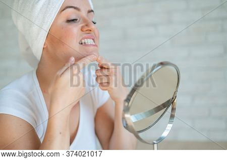 A Woman Looks In A Table Mirror And Crushes Acne On Her Chin. An Unhappy Girl With Problem Skin Does