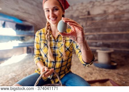 Happy farmer woman showing egg she just collected in a henhouse