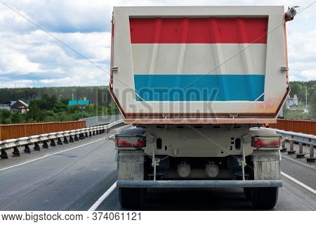 Big Dirty Truck With The National Flag Of Luxembourg
 Moving On The Highway, Against The Background 