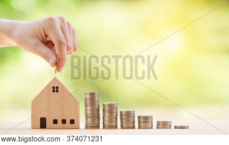 Hand Putting Cion In House Biggy Bank And Stack Of Coins On Wooden Panel. Saving Money Financial For