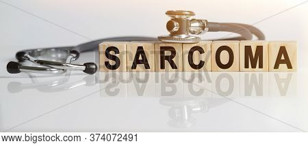 Sarcoma The Word On Wooden Cubes, Cubes Stand On A Reflective White Surface, On Cubes - A Stethoscop