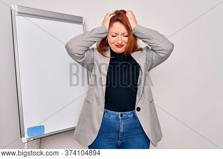 Young beautiful redhead businesswoman doing business presentation using magnetic board suffering from headache desperate and stressed because pain and migraine. Hands on head.