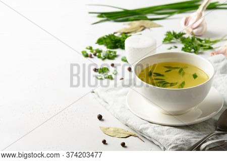 Chicken Broth With , Greens, Garlec, Parsley, Onion In White Bowl On White Table. Copy Space. Close 