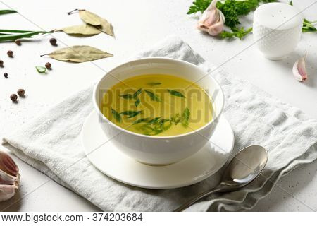 Chicken Broth With , Greens, Garlec, Parsley, Onion In White Bowl On White Table. Copy Space. Close 