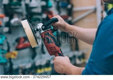 A Man Holds A Polishing Machine In His Hand. A Buyer In A Hardware Store Selects A Product.