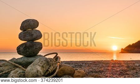 Beach Stone Fireplace With Rope At Sunrise. Sea Water With Rocks In The Background. Vlychada Beach P