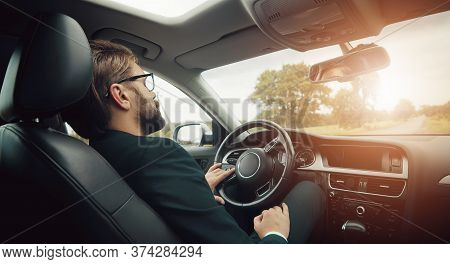 Rear View Of Businessman Resting Or Sleeping On Drivers Seat Staying In Car On Country Roadside