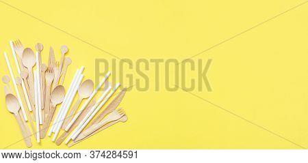 Set Of Wooden Cutlery And White Paper Straws Scattered On A Yellow Background. Ecological Product. E