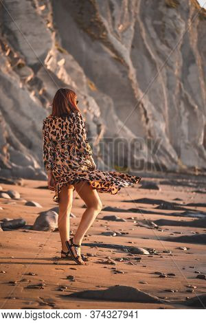 Summer Street Style On A Beach Next To Rocks Of A Young Brunette Caucasian Woman In A Leopard Dress.