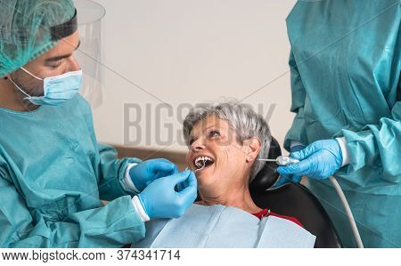 Man Dentist Operating Senior Woman In Dental Clinic - Oral Healthcare Assistance Concept