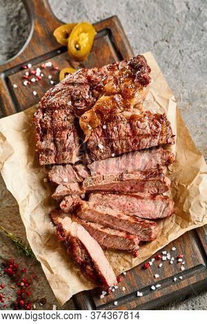 Classic ribeye steak served in waxed paper on wooden cutting board. Cut against grain beef steak. Roasted beef steak with yellow chilli pepper slices and salt crumbs. Rustic spoon and spice bowl