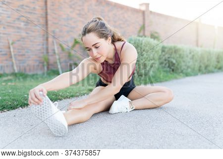 Pretty Young Woman Touching Feet While Doing Warm Up Exercise In Park