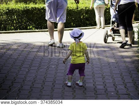A Kid In Yellow T Shirt Follow Parents In A Park In Summer