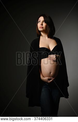 Brunette Pregnant Woman In Black Shawl, Pants And Bra, Bare Belly. She Looking Aside, Posing Sideway