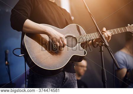 The Singer, Dressed In Black Badlon And Jeans, At The Concert Plays A Guitar Of Dark Color, Connecte