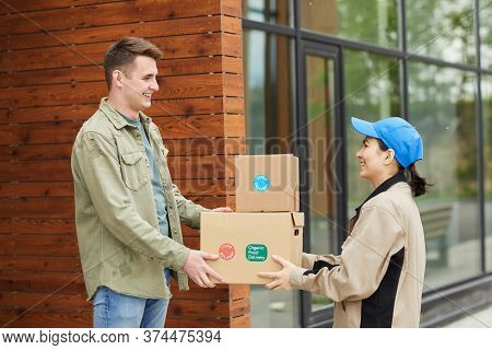 Young Man Getting His Parcels From The Courier While They Standing Outdoors