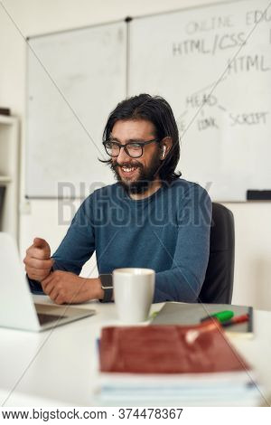 Happy Male Teacher Sitting At His Workplace And Teaching Html Css Online, Looking At Computer Screen