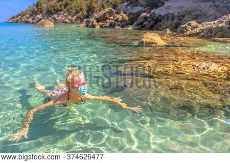 Italian Girl Swims In Fetovaia Beach Sea Wearing Medical Mask During Covid-19. Blonde Woman Having A