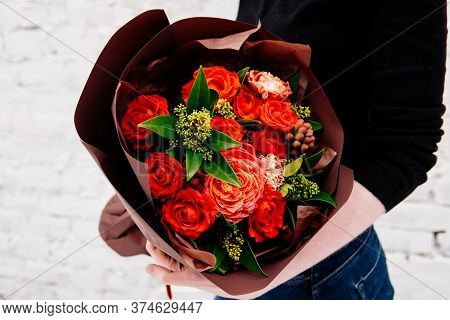 Bouquet Of Flowers In Burgundy Package In The Hands Of A Woman Florist On Background A White Brick W