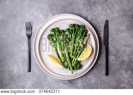 Roasted Broccolini With Lemon On The Plate With Black Cutlery On Stone Table. Top View.