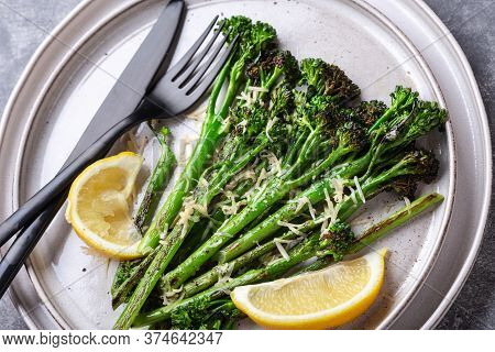 Roasted Broccolini With Lemon On The Plate With Black Cutlery. Angle View.