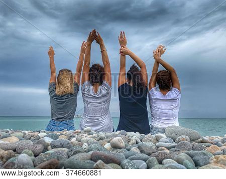 Girls Are Sitting On The Seashore Against The Backdrop Of A Beautiful Sky. They Have Fun Together, D
