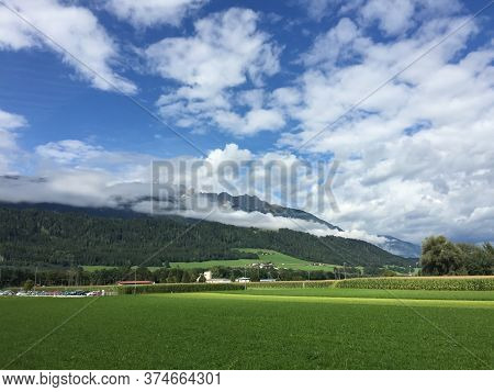 A Gentle Green Field Spreads Out Against The Background Of The High Mountains Of Austria. In Which C