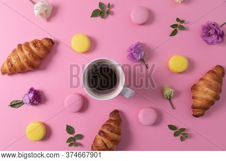 Croissants And Macarons With Flowers And Cup Of Coffee On Pink Background. Top View