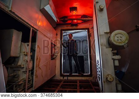 Man In Gateway Corridor Of Airlock Of Abandoned Bunker. Big Hermetic Door Illuminated By Red Lantern