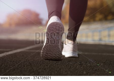 A Man Is Running In The Stadium In Sneakers In The Setting Sun.
