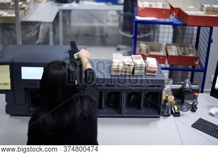 Bank employees using money counting machine while sorting and counting paper banknotes inside bank vault. Large amounts of money in the bank