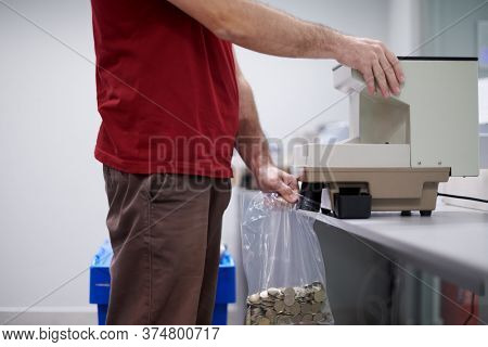 Bank employees using money counting machine while sorting and counting small iron banknotes inside bank vault. Large amounts of money in the bank