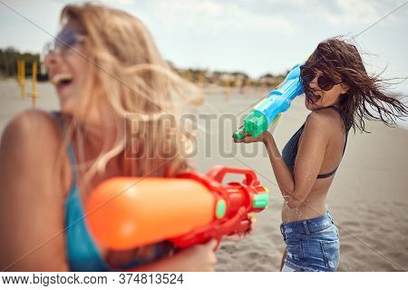 young adult blonde and brunette having fun with water-guns on a sandy beach