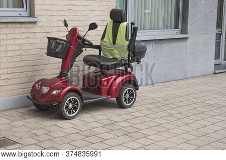 A Red Four Wheel Scooter With A Yellow Fluor Vest Parked Against The Facade Of A House