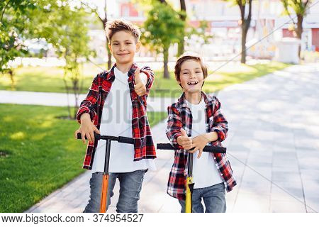 Two Attractive European Boys Brothers, Wearing Red And White Checkered Flannek Shirts, Standing On S