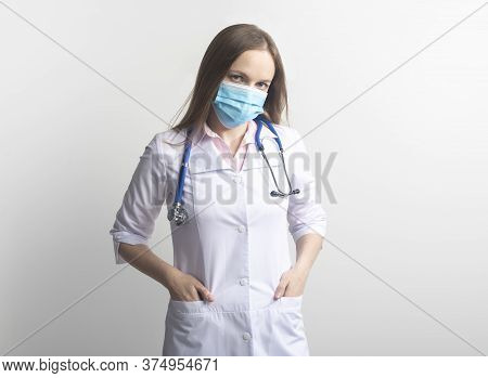 Serious Female Young Caucasian Doctor Wearing Facial Mask And Uniform With Stethoscope Over White Ba