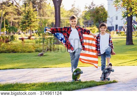 America's Usa Independence Day. Two Cute Brothers Guy Americans Standing In A City Park On Skateboar