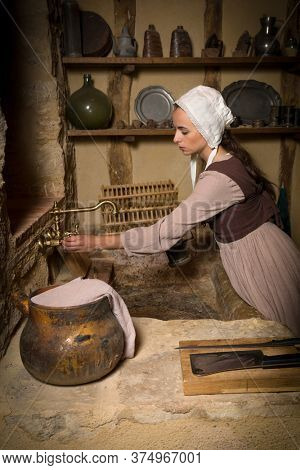 Young woman in Medieval peasant constume working in an authentic antique kitchen in a property released French chateau