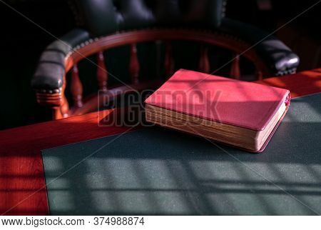 Closed Bible On The Edge Of Table With Chesterfield Chair At The Background. Light Play Forming Line
