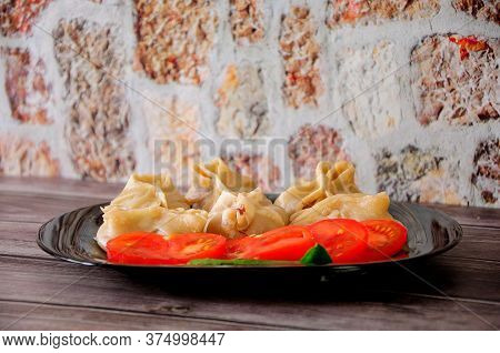 A Plate With Fresh Manti, Tomato And A Leaf Of Salad Stands On A Wooden Table.