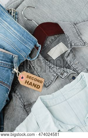 Stack Of Blue Jeans, Shirts And Tag With Inscription Second Hand. Second Hand Clothing Shop. Circula